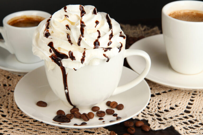 A cup of whipped cream coffee with chocolate drizzle on wooden table