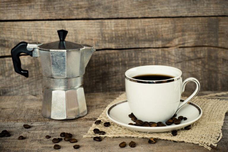 moka pot with a cup of coffee and roasted beans
