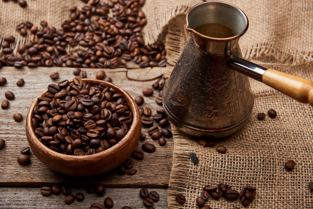 Cezve near coffee beans in bowl on wooden background